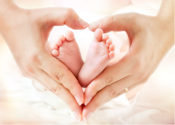Babyfüsse, di von Händen in Herzform gehalten werden